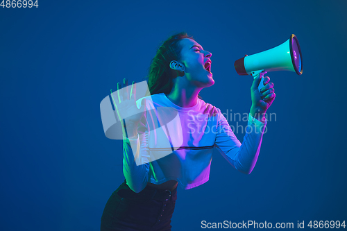 Image of Caucasian woman\'s portrait isolated on blue studio background in pink-green neon light, stylish and beautiful