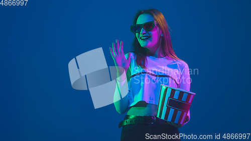 Image of Caucasian woman\'s portrait isolated on blue studio background in pink-green neon light, stylish and beautiful, cinema concept