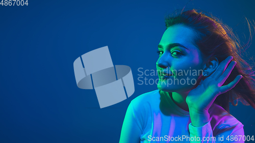 Image of Caucasian woman\'s portrait isolated on blue studio background in pink-green neon light, stylish and beautiful