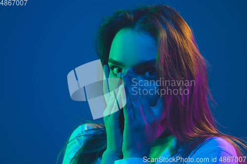 Image of Caucasian woman\'s portrait isolated on blue studio background in pink-green neon light, stylish and beautiful