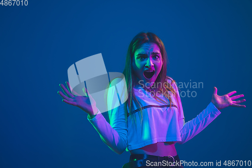 Image of Caucasian woman\'s portrait isolated on blue studio background in pink-green neon light, stylish and beautiful