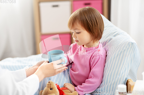 Image of doctor giving hot tea to sick little girl in bed