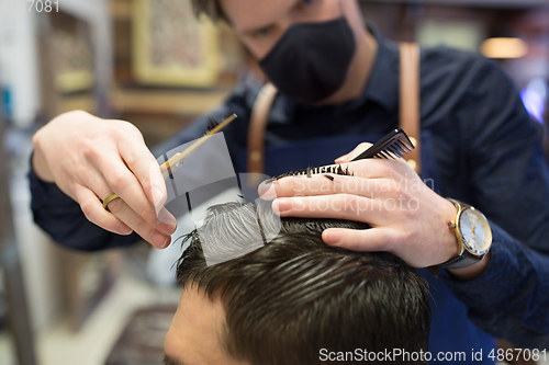 Image of male hairdresser cutting hair at barbershop