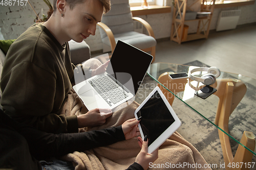 Image of Attractive young couple using devices together, tablet, laptop, smartphone, headphones wireless. Gadgets and technologies connecting people all around the world