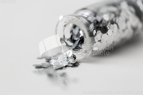 Image of silver glitters poured from small glass bottle