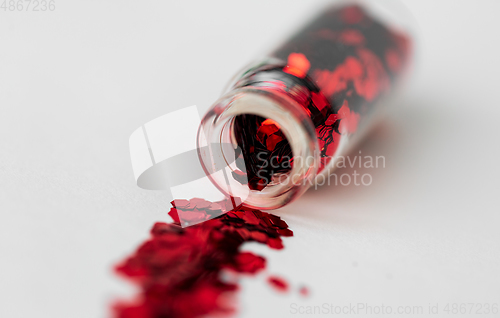 Image of red glitters poured from small glass bottle