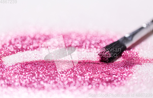 Image of make up brush making stroke on pink glitters