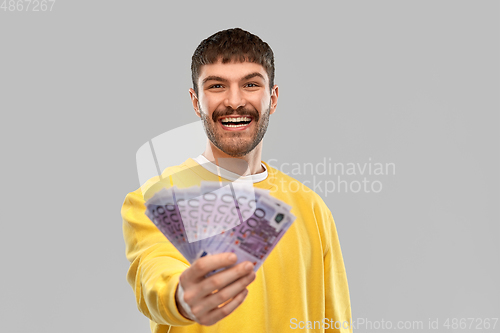 Image of smiling young man in yellow sweatshirt with money