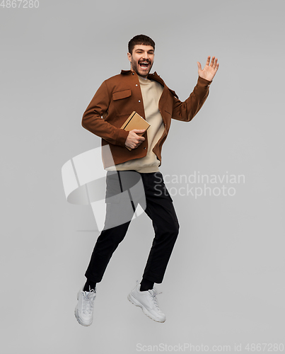 Image of happy smiling young man with diary jumping in air