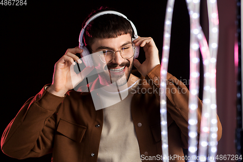 Image of man in headphones over neon lights of night club