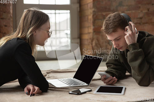 Image of Attractive young couple using devices together, tablet, laptop, smartphone, headphones wireless. Gadgets and technologies connecting people all around the world