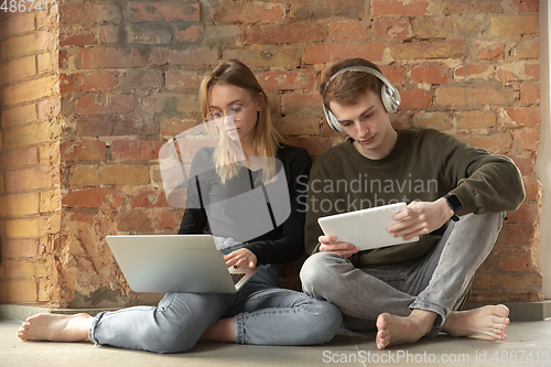 Image of Attractive young couple using devices together, tablet, laptop, smartphone, headphones wireless. Gadgets and technologies connecting people all around the world