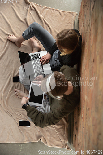 Image of Attractive young couple using devices together, tablet, laptop, smartphone, headphones wireless. Gadgets and technologies connecting people all around the world. Top view