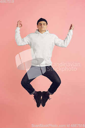 Image of Caucasian young man\'s modern portrait on pink studio background in high jump