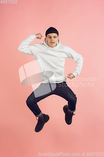 Image of Caucasian young man\'s modern portrait on pink studio background in high jump