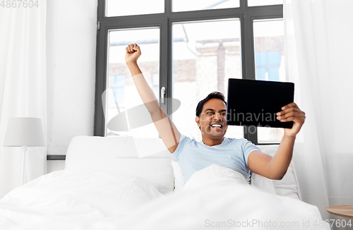 Image of happy indian man with tablet pc in bed at home
