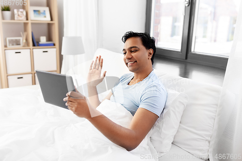 Image of happy man with tablet pc in bed having video call