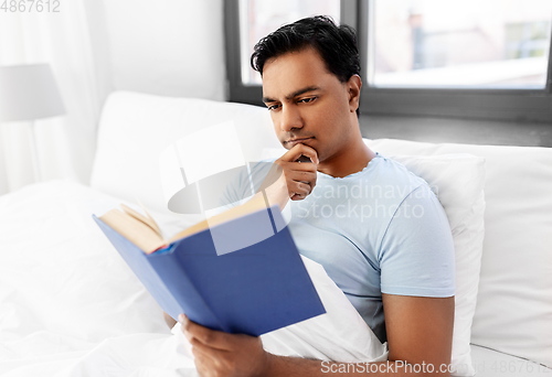 Image of indian man reading book in bed at home