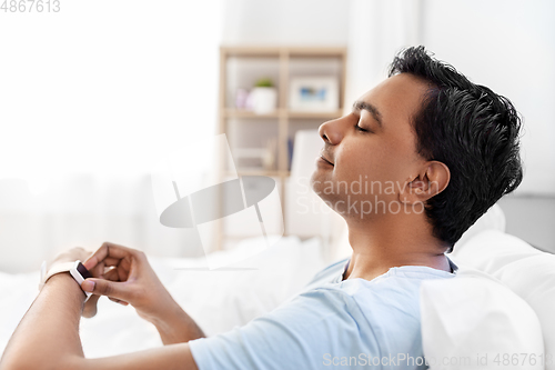 Image of happy indian man with smart watch in bed at home