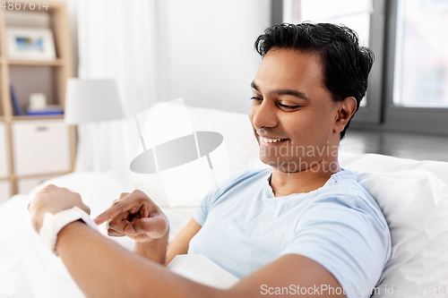 Image of happy indian man with smart watch in bed at home