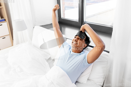 Image of happy smiling indian man lying in bed at home