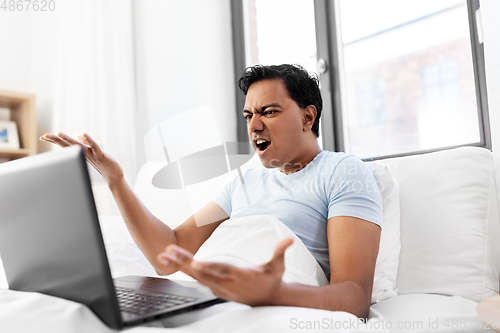 Image of angry indian man with laptop in bed at home