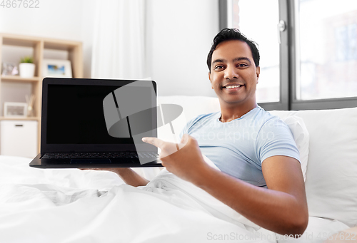 Image of happy indian man showing his laptop in bed at home