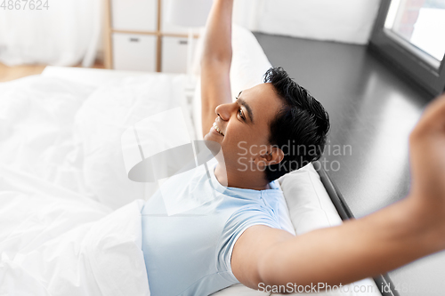 Image of happy smiling indian man lying in bed at home