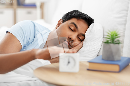 Image of sleepy indian man with alarm clock lying in bed