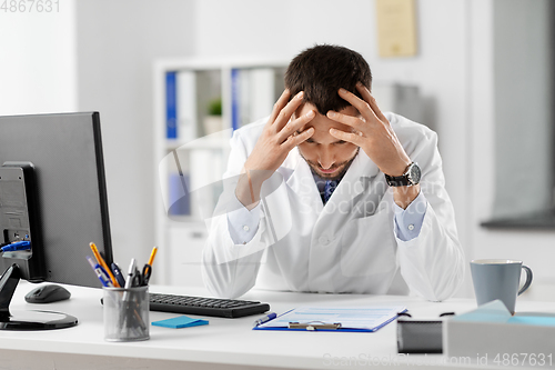 Image of stressed male doctor with clipboard at hospital