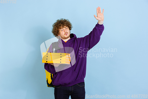 Image of Contacless delivery service during quarantine. Man delivers food and shopping bags during insulation. Emotions of deliveryman isolated on blue background.