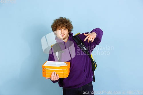 Image of Contacless delivery service during quarantine. Man delivers food and shopping bags during insulation. Emotions of deliveryman isolated on blue background.