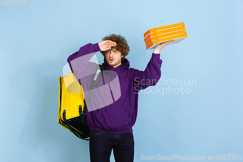 Image of Contacless delivery service during quarantine. Man delivers food and shopping bags during insulation. Emotions of deliveryman isolated on blue background.