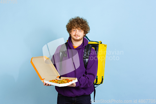 Image of Contacless delivery service during quarantine. Man delivers food and shopping bags during insulation. Emotions of deliveryman isolated on blue background.