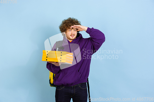 Image of Contacless delivery service during quarantine. Man delivers food and shopping bags during insulation. Emotions of deliveryman isolated on blue background.