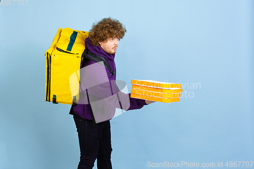 Image of Contacless delivery service during quarantine. Man delivers food and shopping bags during insulation. Emotions of deliveryman isolated on blue background.