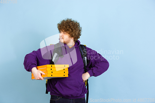 Image of Contacless delivery service during quarantine. Man delivers food and shopping bags during insulation. Emotions of deliveryman isolated on blue background.