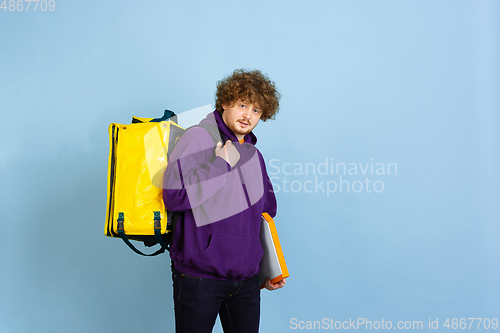 Image of Contacless delivery service during quarantine. Man delivers food and shopping bags during insulation. Emotions of deliveryman isolated on blue background.