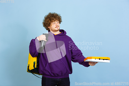 Image of Contacless delivery service during quarantine. Man delivers food and shopping bags during insulation. Emotions of deliveryman isolated on blue background.