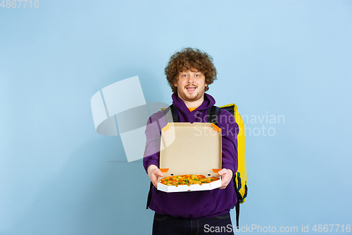 Image of Contacless delivery service during quarantine. Man delivers food and shopping bags during insulation. Emotions of deliveryman isolated on blue background.