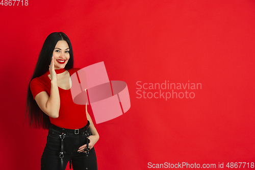 Image of Caucasian young woman\'s monochrome portrait on red studio background, emotional and expressive