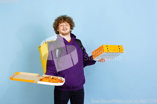 Image of Contacless delivery service during quarantine. Man delivers food and shopping bags during insulation. Emotions of deliveryman isolated on blue background.