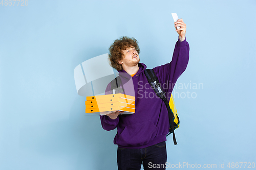 Image of Contacless delivery service during quarantine. Man delivers food and shopping bags during insulation. Emotions of deliveryman isolated on blue background.