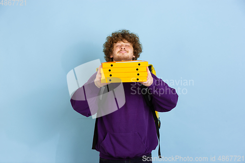 Image of Contacless delivery service during quarantine. Man delivers food and shopping bags during insulation. Emotions of deliveryman isolated on blue background.