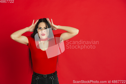Image of Caucasian young woman\'s monochrome portrait on red studio background, emotional and expressive