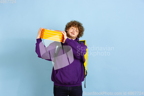 Image of Contacless delivery service during quarantine. Man delivers food and shopping bags during insulation. Emotions of deliveryman isolated on blue background.