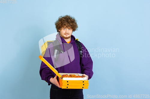 Image of Contacless delivery service during quarantine. Man delivers food and shopping bags during insulation. Emotions of deliveryman isolated on blue background.