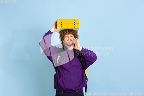 Image of Contacless delivery service during quarantine. Man delivers food and shopping bags during insulation. Emotions of deliveryman isolated on blue background.