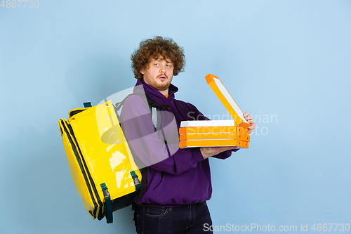 Image of Contacless delivery service during quarantine. Man delivers food and shopping bags during insulation. Emotions of deliveryman isolated on blue background.