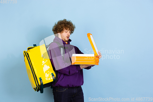 Image of Contacless delivery service during quarantine. Man delivers food and shopping bags during insulation. Emotions of deliveryman isolated on blue background.